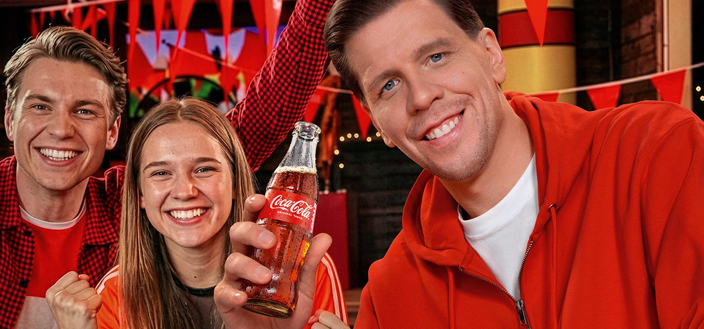 Radosny tłum z kibicem pijącym Coca-Cola i logo FIFA World Cup 26™ w tle.